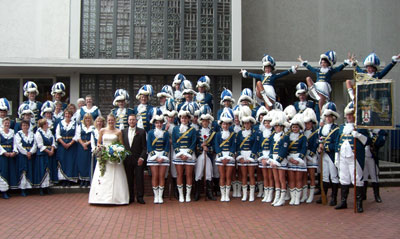 Das Foto zeigt vorne das Brautpaar, im Hintergrund die Karnevalsgesellschaft Blau-Weiß