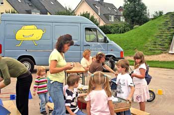 Das Bild zeigt eine Betreuerin mit mehreren Kindern vor dem Spielmobil