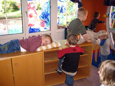 Das Foto zeigt sechs kleine Kinder, eins schläft, im Hintergrund hängen bunte selbstgemalte Bilder