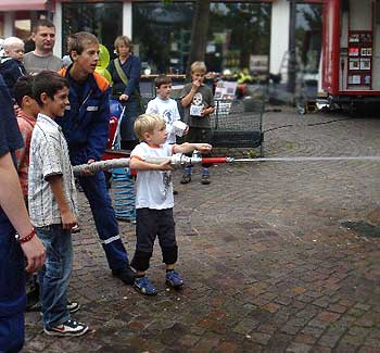 Das Bild zeigt einen kleinen Jungen, der einen Feuerwehrschlauch hält.
