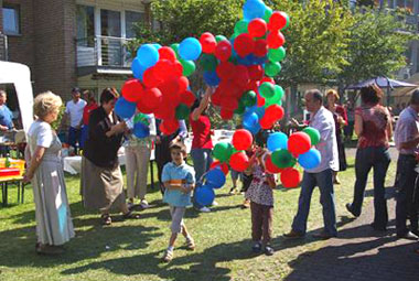 Das Foto zeigt Gäste beim Sommerfest auf dem Rasen, in der Mitte viele Luftballons