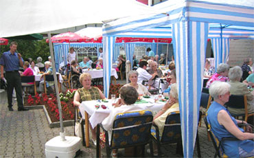 Das Foto zeigt viele Seniorinnen an Tischen unter Pavillons beim Sommerfest