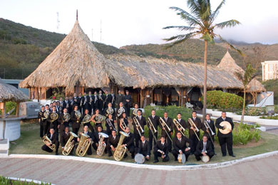 Das Foto zeigt das Orchester Venezuelan Brass Ensemble vor einer mit Stroh gedeckten Hütte