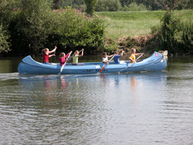 Das Foto zeigt ein blaues Kanu mit sechs Kindern auf der Sieg