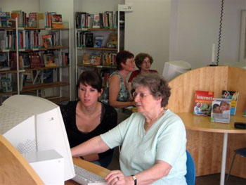 Eine Mitarbeiterin der Bibliothek hilft einer Seniorin am Computer