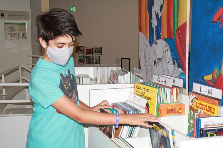 2020-06-24_adrian-abilleira Junge mit Mundschutz blättert durch Comics in einem Regal