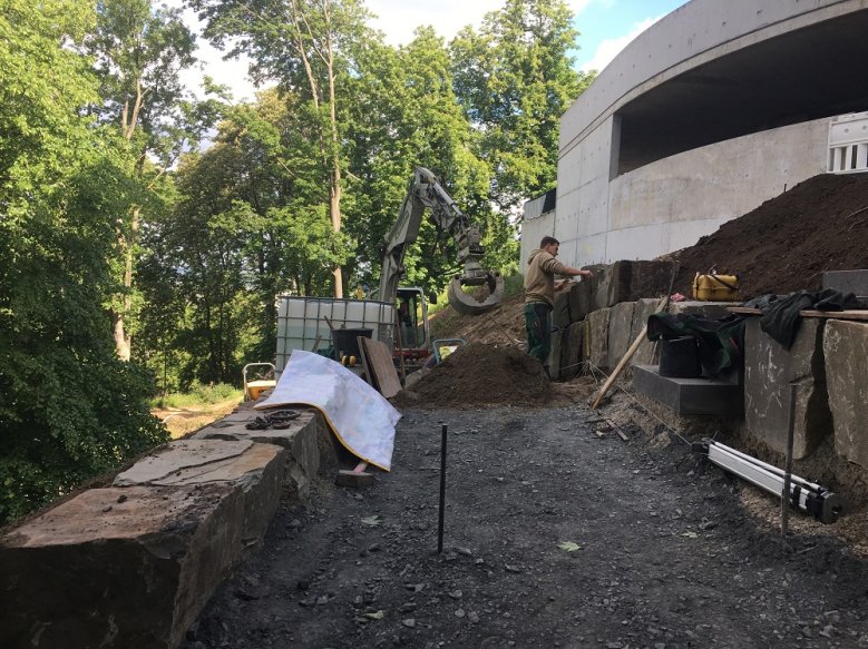2020-05-14_Michaelsberg Bauarbeiter und Bagger zwischen großen Felsblöcken, die einen geschotterten Weg einrahmen