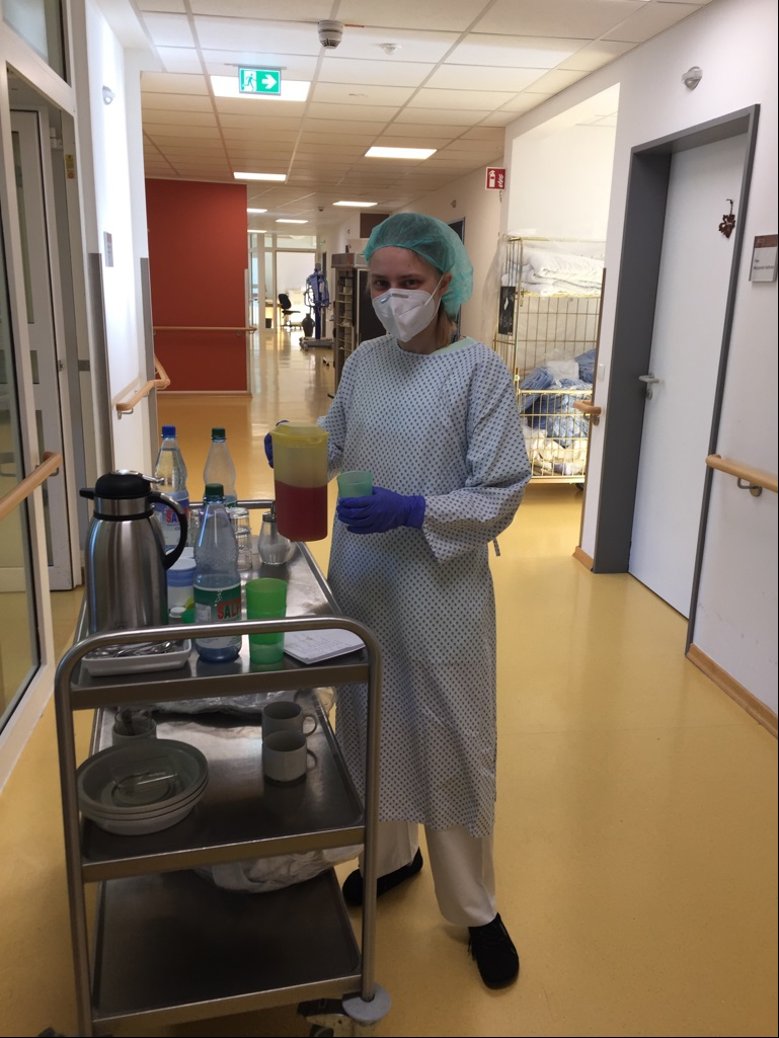 2020-05-15_Prautsch Pflegekraft mit Schürze, Mund-Nase-Maske und Haarnetz an einem Servierwagen