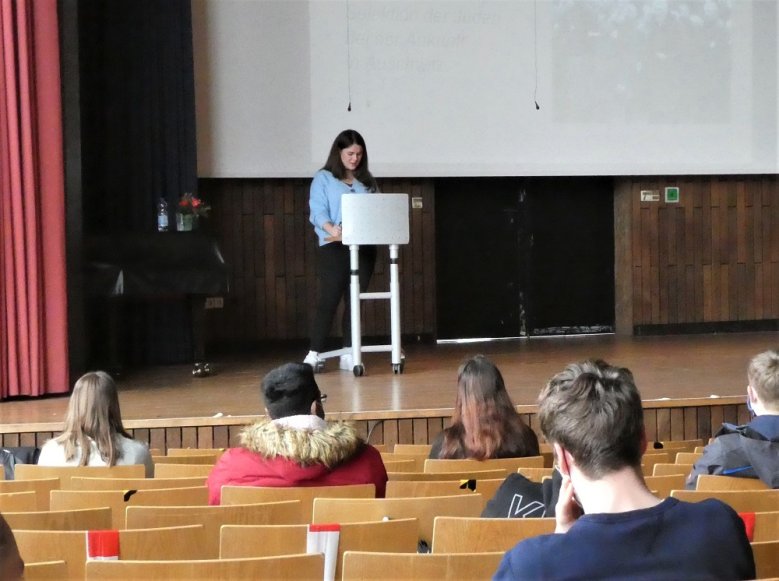 2020-11-11_melissa-quint-anno-gymnasium Junge Frau am Rednerpult vor jüngeren Zuhörern