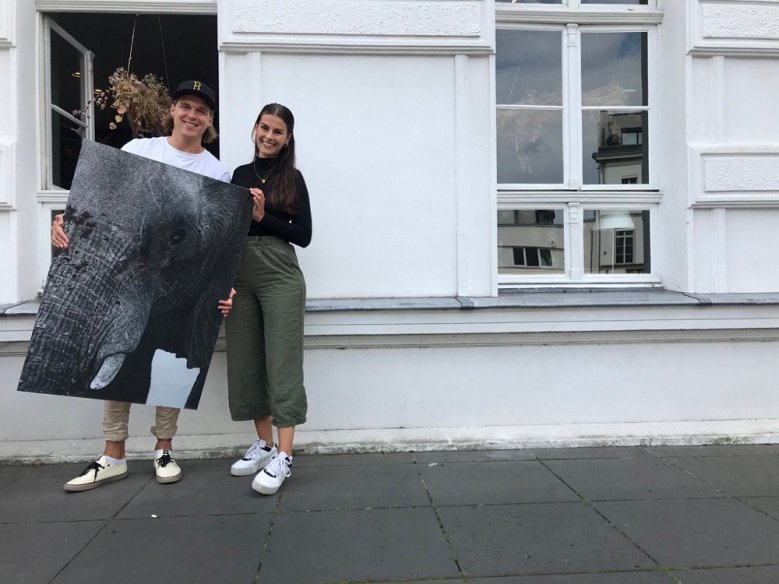 2020-09-02_muca Ein junger Mann, neben einer jungen Frau stehend, hält ein Schwarz-Weiß-Portrait eines Elephanten in der Hand.