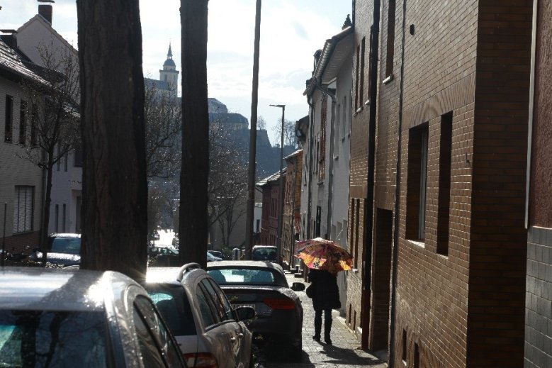 Aprilwetter Person mit Regenschirm neben zwischen Häusern und Autos, in denen sich die Sonne spiegelt, mit Blick auf den Michaelsberg
