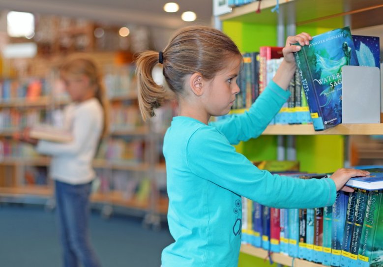 2020-09-01_bibliothek Ein Mädchen nimmt sich ein Buch aus einem Bibliotheksregal.