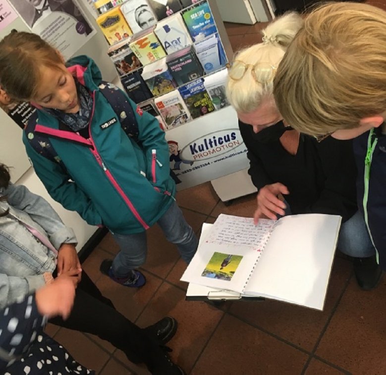 Touristinfo Grundschüler und Mitarbeiterin der Tourist Information bei der Begutachtung einer von den Kindern erstellten Broschüre.