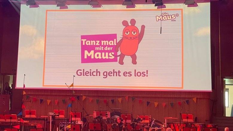Hans Alfred Keller-Schule: Tanz mal mit der Maus Leinwand mit dem Schriftzug "Tanz mal mit der Maus - Gleich geht es los!" über einem Orchesteraufbau.