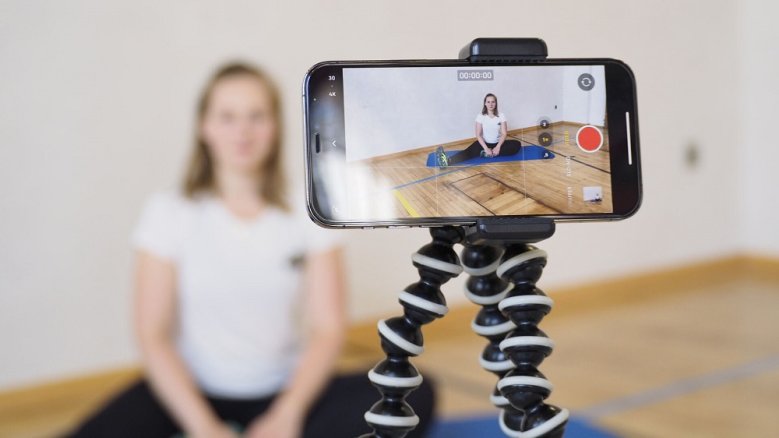 VHS Online-Yoga Smartphone auf einem Stativ, das die Yoga-Einheit einer Dozentin aufzeichnet