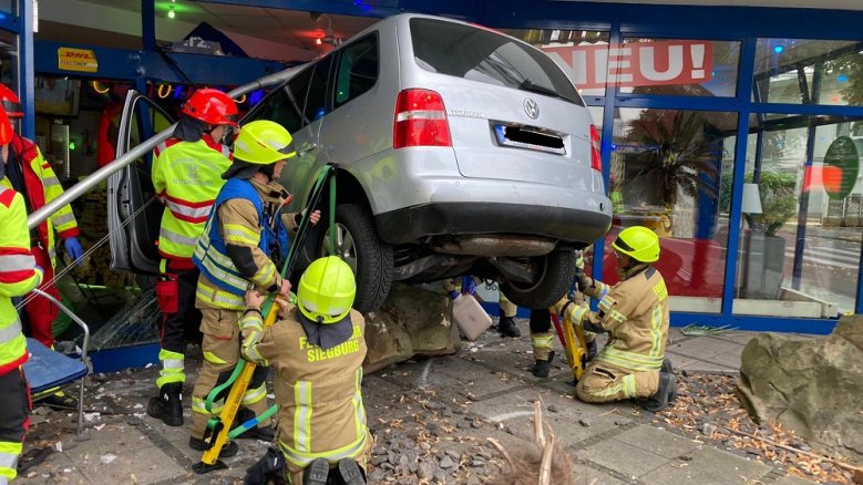 Unfall Sonnenstudio Feuerwehrleute an einem Auto, das, auf einem Stein stehend, in der Fensterfront eines Sonnenstudios steckt.