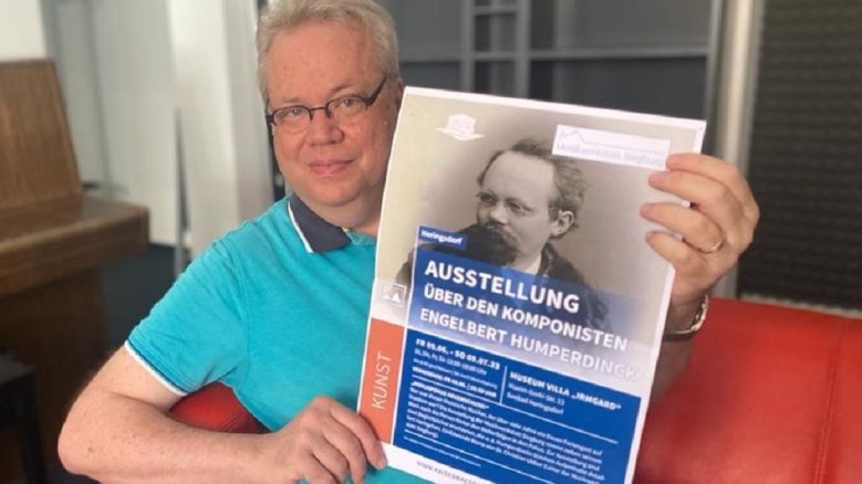 Humperdinck Usedom Dr. Christian Ubber, Leiter der Musikwerkstatt, mit dem Ausstellungsplakat zur Ausstellung "Hokuspokus Hexenschuss - Der Komponist Engelbert Humperdinck" in Heringsdorf.
