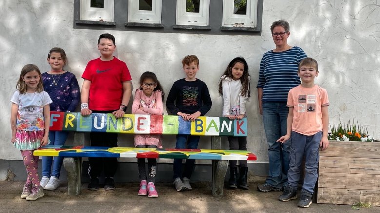 Adolf-Kolping-Schule Freundebank Schülerinnen und Schüler sowie eine Lehrerin an der bunt bemalten "Freunde-Bank".