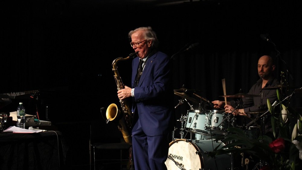 Saxophon spielender Klaus Doldinger im blauen Anzug, dahinter ein Schlagzeuger