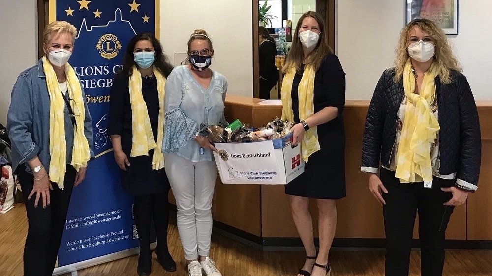 Fünf Frauen mit Mund-Nase-Bedeckung übergeben einen Karton mit Lebensmitteln