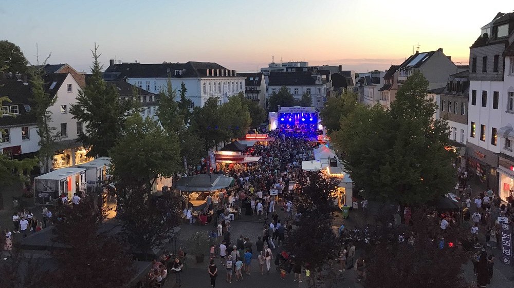 Luftbild von Menschen vor einer ausgeleuchteten Bühne auf dem Siegburger Markt, im Hintergrund Abendhimmel