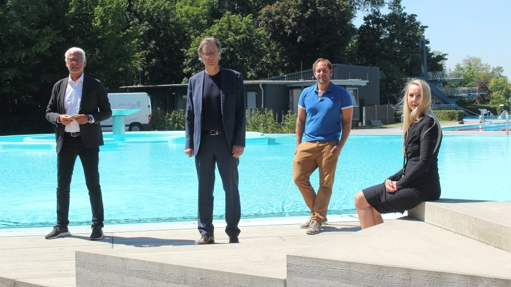 Drei Männer stehen am Beckenrand eines Schwimmbads, daneben sitzt eine Frau