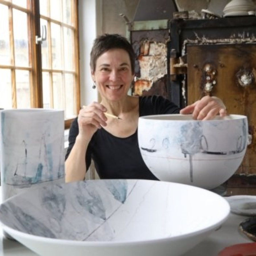 Frau mit Pinsel in der Hand zwischen großen Keramikvasen und -schalen
