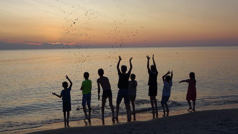Kinder als Schattenumriss bei Sonnenuntergang am Strand