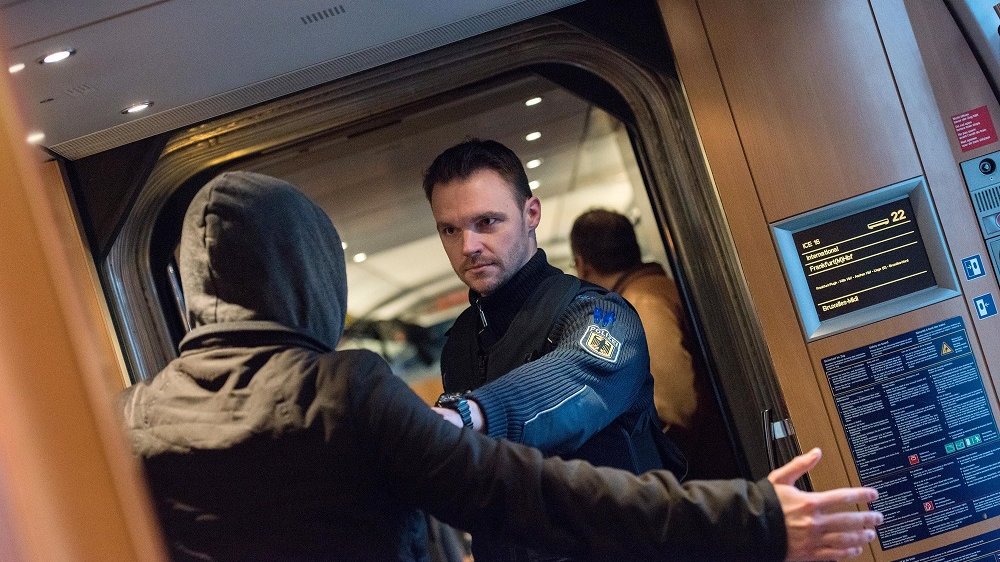 Bundespolizist hält in einem Zug mit ausgestrecktem Arm einen offenbar aggressiven jungen Mann mit Kapuze von sich fern.