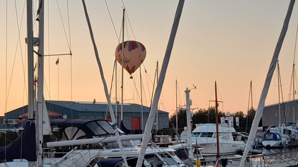 Heißluftballon am Abendhimmel über im Hafen vertäuten Segelbooten