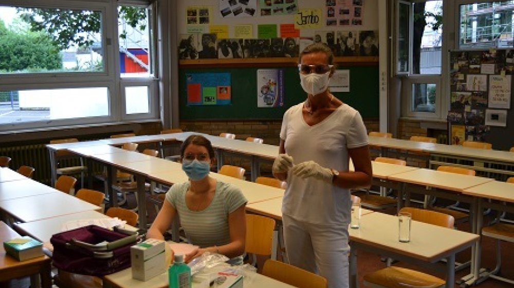 Zwei Arztinnen mit Mund-Nase-Bedeckung in einem Klassenzimmer.