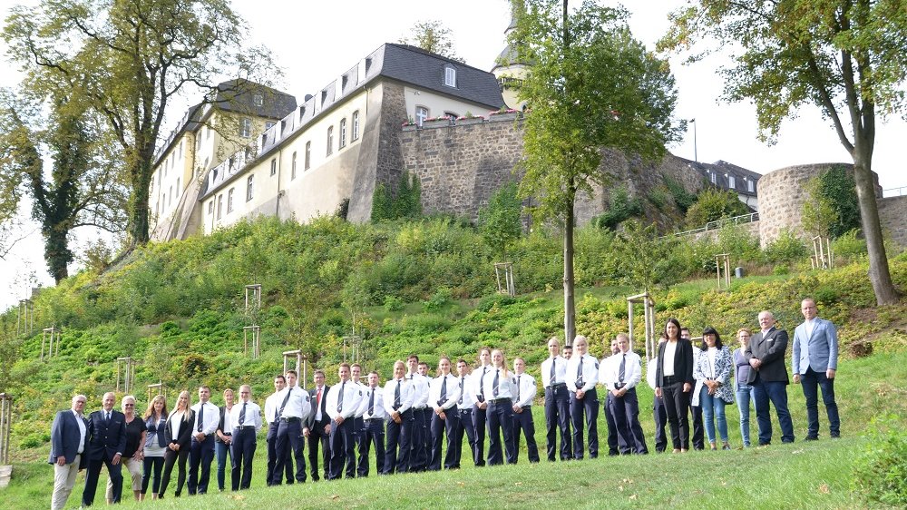 Gruppenfoto junger Polizistinnen und Polizisten auf der Wiese am Michaelsberg mit Blick auf das ehemalige Klostergebäude.