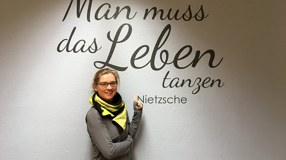Ulli Hartmann vor einer Leinwand mit Nietzsches Zitat "Man muss das Leben tanzen”
