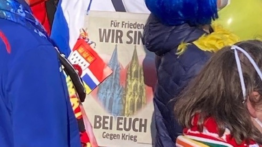 Verkleidete Menschen, einer trägt ein Plakat "Für Frieden - Wir sind bei euch - Gegen Krieg"
