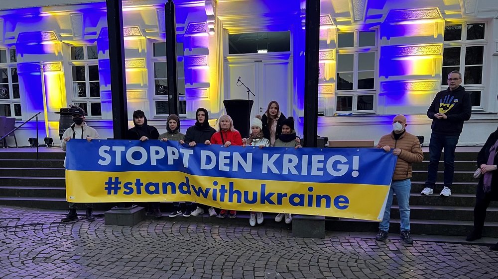 Ukrainische Flüchtlingsgruppe und weitere Personen mit einem Banner "Stoppt den Krieg! #standwithukraine"