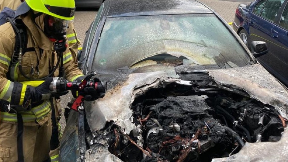 Feuerwehrmann an einem Auto mit ausgebranntem Motorraum