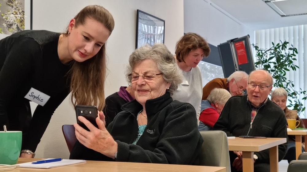 Junge Frau, die einer älteren bei der Bedienung des Smartphones hilft.