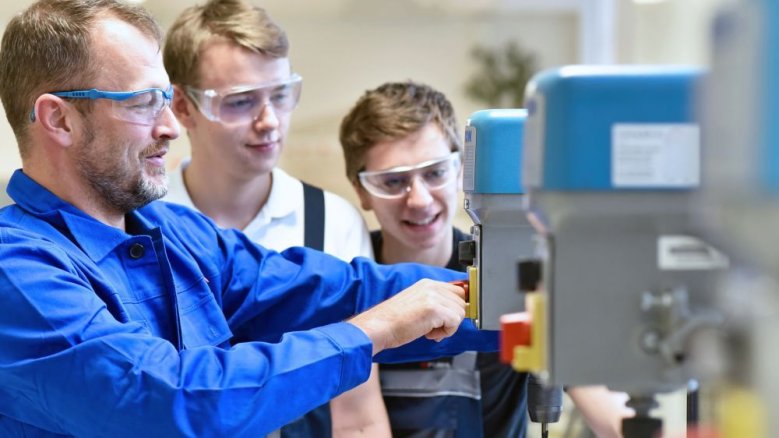 2026-06_Schulhoftournee_AdobeStock_industrieblick Ausbilder und Auszubildende an einer Maschine.